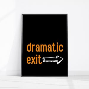 May include: Black framed art print with the words "dramatic exit" in orange, with a white arrow pointing right. The artwork is displayed against a white wall.