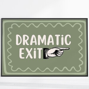 Op de afbeelding: Ingelijste kunstprint met de tekst "DRAMATIC EXIT" in het wit, met een illustratie van een wijzende hand. De achtergrond is saliegroen met een golvende rand, alles in een zwarte lijst.