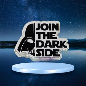 May include: An iridescent pin with Darth Vader's helmet and the words "JOIN THE DARK SIDE" in black. The pin is set on a light blue platform, with a starry night sky in the background.