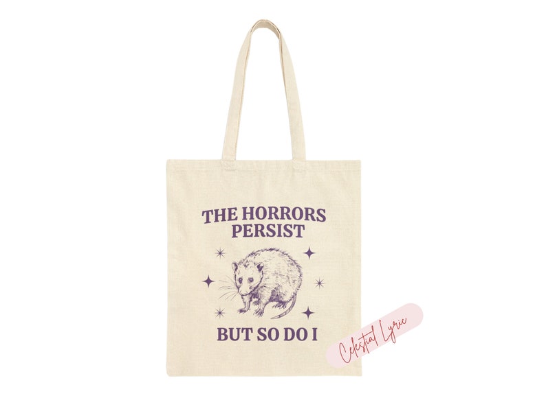 May include: A beige tote bag with a purple graphic of a possum and the text "The Horrors Persist But So Do I".
