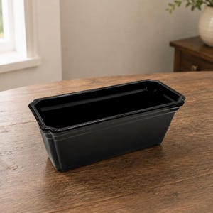 May include: A rectangular black planter with a smooth, glossy finish and a wide, flat rim. The container features slightly tapered sides and a clean, simple design, providing a deep, open interior space for holding various items or plants.