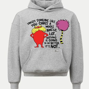 May include: A light gray hoodie featuring a graphic of a red character with yellow hair and a purple tree. The text reads "UNLESS SOMEONE LIKE YOU CARES A WHOLE AWFUL LOT, NOTHING IS GOING TO GET BETTER. IT'S NOT."