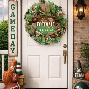 May include: A front door decorated for football season. A wreath with footballs and the text "Hello Football Season" hangs on the door. A sign that says "Gameday" hangs to the left. Other decorations include a foam finger, footballs, and a helmet.