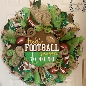 May include: A decorative football-themed wreath with green, brown, and tan mesh. The wreath features miniature footballs, ribbons, and a central sign that reads "Hello FOOTBALL Season" with yard markers. A festive decoration for the football season.