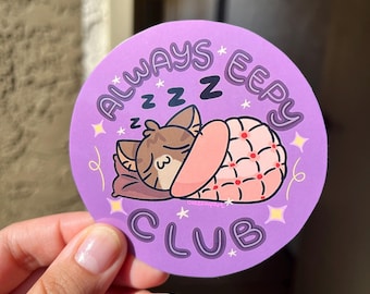 May include: Purple round sticker with the text "Always Eeepy Club" in a white outline. The sticker features a cartoon cat sleeping in a pink and red blanket with the text "zzz" above it.