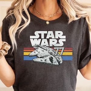Può includere: Una maglietta grigio scuro con una grafica di Star Wars in stile vintage. La grafica presenta la nave spaziale Millennium Falcon e il testo "Star Wars 77".