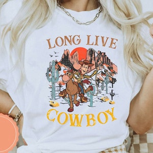 Pu&ograve; includere: Maglietta bianca con una grafica di Woody di Toy Story a cavallo in un paesaggio desertico. Il testo "Long Live Cowboy" &egrave; stampato sulla maglietta.