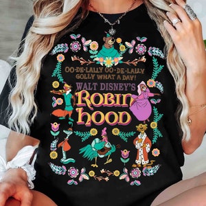 May include: Black t-shirt with a colorful graphic of characters from the Disney movie Robin Hood. The graphic includes Robin Hood, Little John, Maid Marian, and the Sheriff of Nottingham. The text "OO-DE-LALLY OO-DE-LALLY GOLLY WHAT A DAY! WALT DISNEY'S ROBIN HOOD" is printed on the shirt.