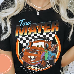 May include: Black t-shirt featuring a cartoon image of Tow Mater from the Cars movie. The design includes the text "Tow Mater" above the character, with a checkered flag and a colorful circular background.