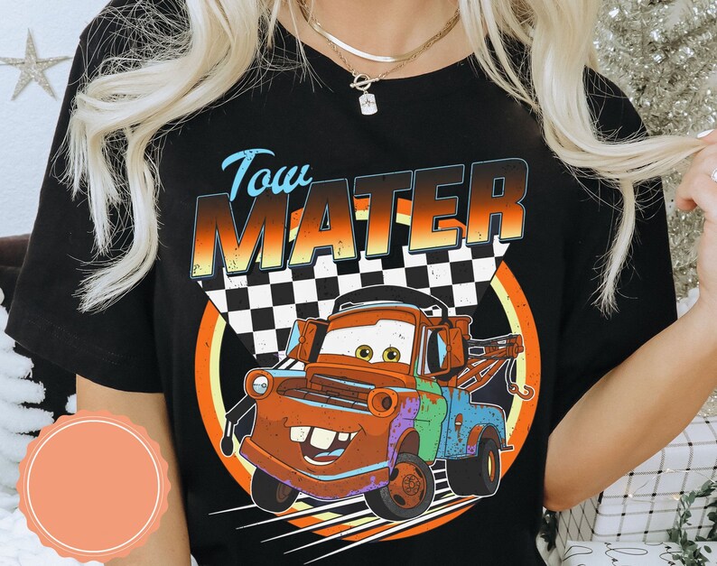 May include: Black t-shirt featuring a cartoon image of Tow Mater from the Cars movie. The design includes the text "Tow Mater" above the character, with a checkered flag and a colorful circular background.