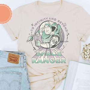 Puede incluir: Una camiseta beige con una imagen de dibujos animados de Buzz Lightyear de Toy Story. El texto "To Infinity and Beyond" est&aacute; por encima de la imagen y "Space Ranger" est&aacute; por debajo de la imagen.