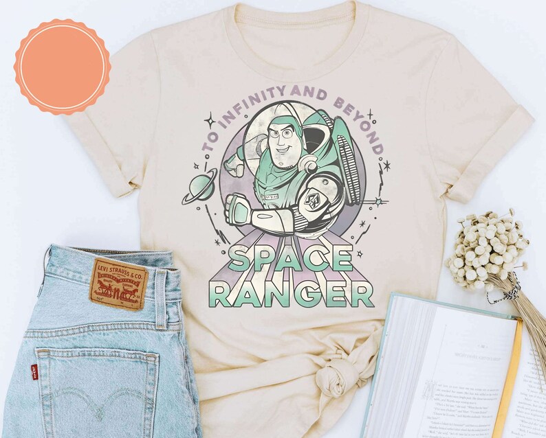 Puede incluir: Una camiseta beige con una imagen de dibujos animados de Buzz Lightyear de Toy Story. El texto "To Infinity and Beyond" est&aacute; por encima de la imagen y "Space Ranger" est&aacute; por debajo de la imagen.