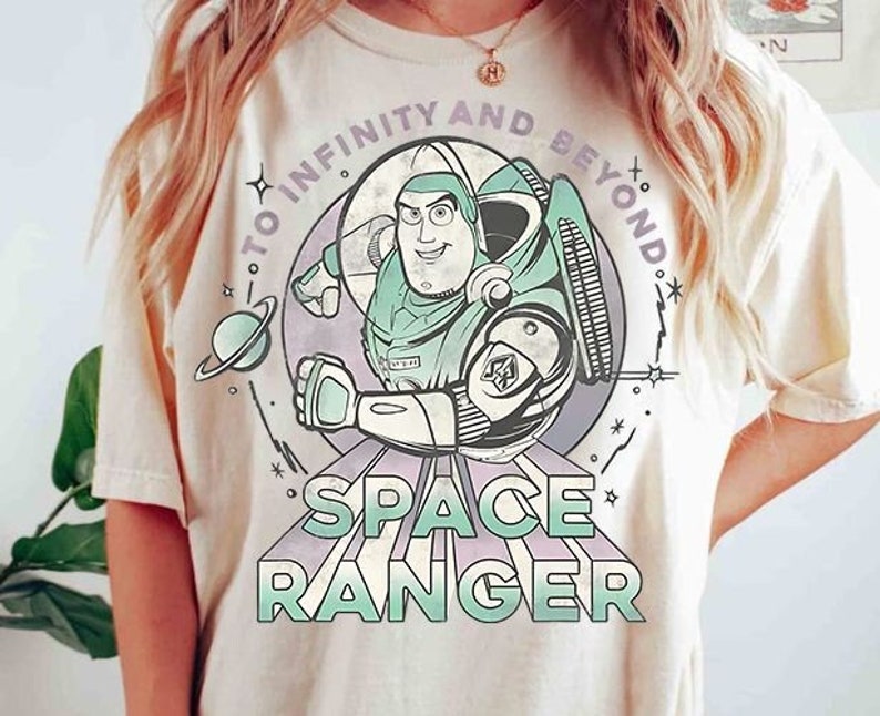 Puede incluir: Una camiseta blanca con una imagen de dibujos animados de Buzz Lightyear de Toy Story. El texto "To Infinity and Beyond" est&aacute; en un c&iacute;rculo alrededor de Buzz. El texto "Space Ranger" est&aacute; debajo de Buzz en una fuente de estilo retro.