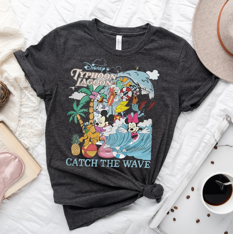 May include: A dark gray t-shirt with a colorful graphic of Mickey Mouse and friends at Disney's Typhoon Lagoon water park. The graphic includes the text "Disney's Typhoon Lagoon" and "Catch the Wave".