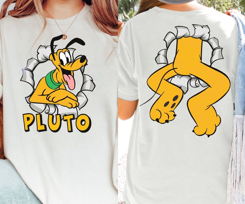 Puede incluir: Camiseta blanca con una imagen de dibujos animados de Pluto el perro asom&aacute;ndose por un agujero rasgado. El texto "PLUTO" est&aacute; impreso debajo de la imagen. La parte posterior de la camiseta muestra las piernas de Pluto asom&aacute;ndose por un agujero rasgado.