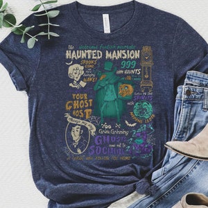 May include: A navy blue t-shirt with a vintage-style graphic design featuring a haunted mansion, ghosts, and the text "The Welcome Foolish Mortals Haunted Mansion 999 Happy Haunts".