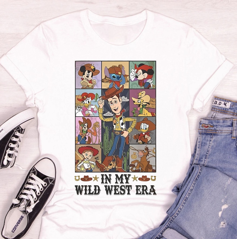 Puede incluir: Camiseta blanca con un estampado gr&aacute;fico colorido de varios personajes de Disney en un tema del oeste. El texto "U* IN MY *U WILD WEST ERA" est&aacute; impreso debajo del gr&aacute;fico.