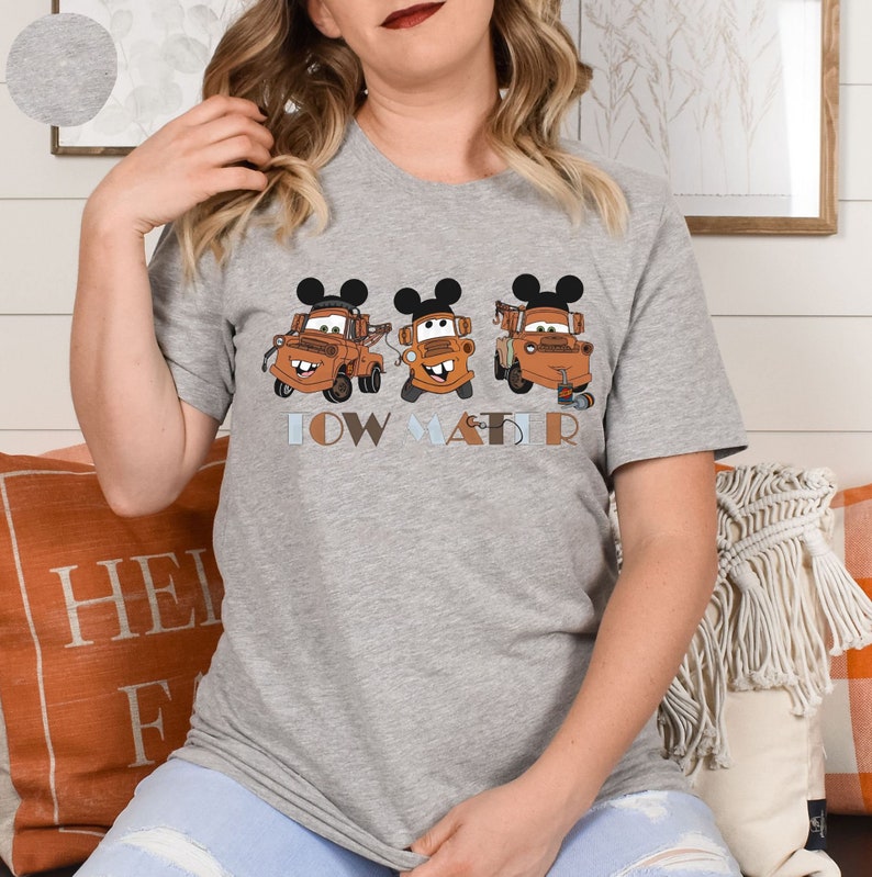 May include: Gray t-shirt with a graphic of three orange tow trucks with Mickey Mouse ears. The text "Tow Mater" is printed below the trucks.