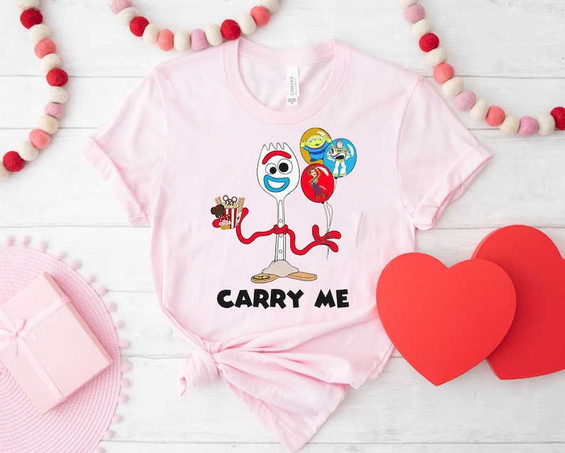 May include: Pink t-shirt with a cartoon image of Forky from Toy Story holding a box of french fries and balloons. The text "Carry Me" is printed below the image.