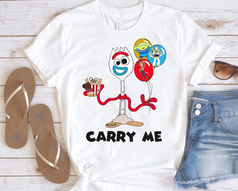 May include: White t-shirt with a cartoon image of Forky from Toy Story. Forky is holding a box of popcorn and a Mickey Mouse ear. He is wearing a red ribbon and the text "Carry Me" is printed below him.
