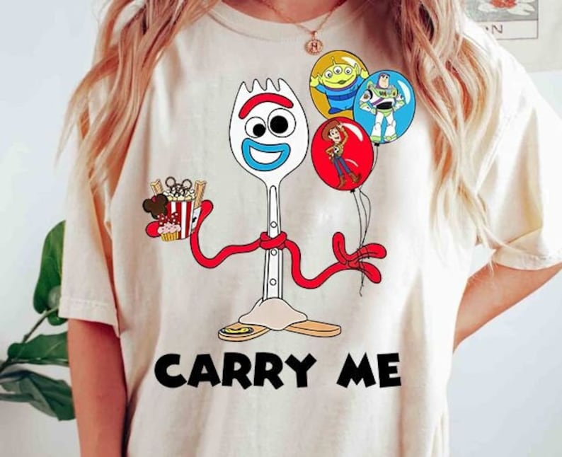 May include: A white t-shirt with a cartoon image of Forky from Toy Story. Forky is holding a bucket of popcorn and has three balloons with images of Buzz Lightyear, Woody, and Alien. The text "Carry Me" is printed below the image.