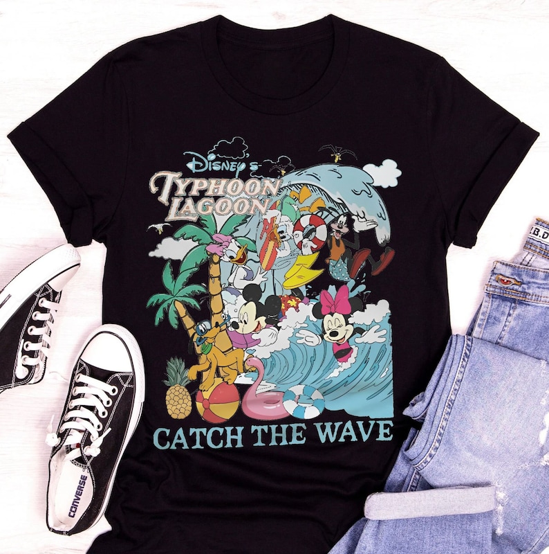 May include: Black t-shirt with a colorful graphic of Mickey Mouse and friends at Disney's Typhoon Lagoon water park. The graphic includes a wave, palm trees, a pineapple, and a beach ball. The text "Catch the Wave" is printed below the graphic.