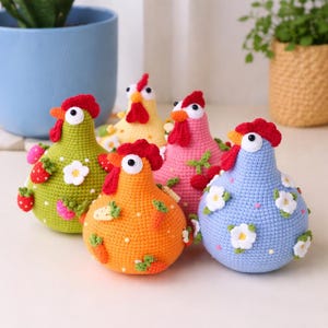 May include: A collection of five colorful, crocheted chicken figurines. Each chicken has a red comb and wattle, with details like strawberries, carrots, and flowers. The chickens are in shades of green, yellow, pink, orange, and blue.