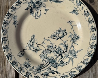 May include: A vintage ceramic plate with a white background and a blue floral design. The plate has a scalloped edge and a decorative border.