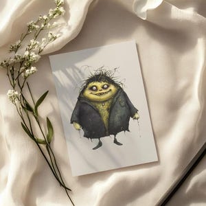 May include: A whimsical illustration of a creature with yellow skin, spiky black hair, and a dark coat. The artwork is on a white card, set against a soft, white fabric with a sprig of white flowers and a black pen.