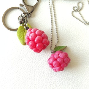 Può includere: Una collana a catena d'argento con un ciondolo a forma di lampone rosa e un portachiavi d'argento con un ciondolo a forma di lampone rosa.
