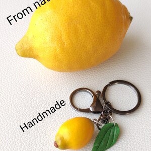 May include: A yellow lemon keychain with a green leaf charm. The keychain is handmade and says "From nature" and "Handmade".