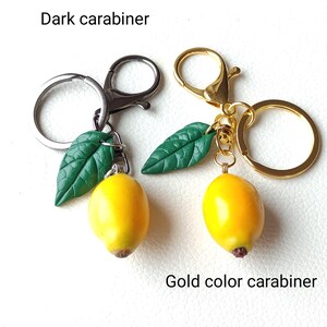 May include: Two lemon keychains with green leaves. One keychain has a dark carabiner and the other has a gold color carabiner.