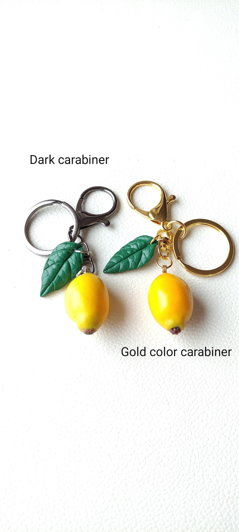 May include: Two lemon keychains with green leaves. One keychain has a dark carabiner and the other has a gold color carabiner.