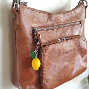 Handmade lemon keychain with a green leaf, attached to a brown leather bag. The realistic fruit charm adds a playful and stylish touch, making it a unique accessory for purses, backpacks, or keys