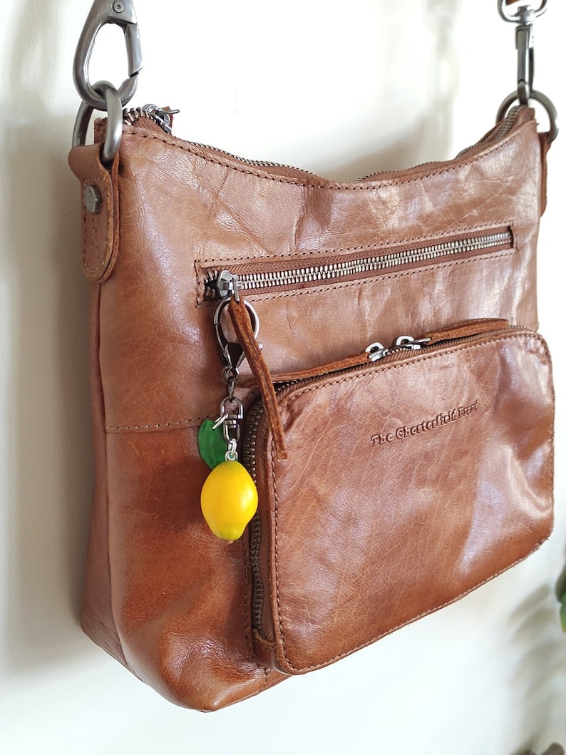 Handmade lemon keychain with a green leaf, attached to a brown leather bag. The realistic fruit charm adds a playful and stylish touch, making it a unique accessory for purses, backpacks, or keys