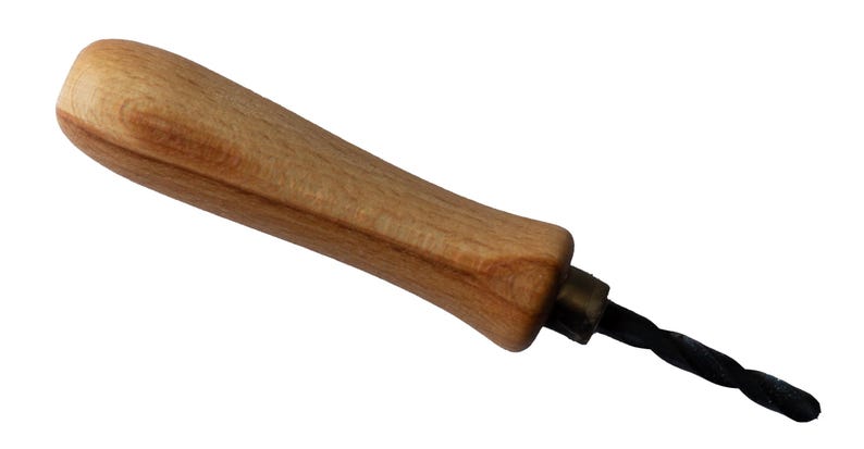 May include: A woodworking tool with a light brown wooden handle and a black, twisted metal drill bit. The handle is smooth and ergonomic, designed for a comfortable grip. The tool is likely used for drilling holes in wood.