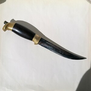 Peut inclure: Un couteau de chasse à manche noir et lame argentée. Le couteau a une pointe arrondie et une lame légèrement incurvée.