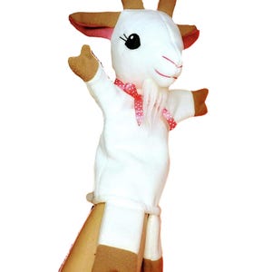 以下が含まれることがあります： 茶色の角、耳、蹄を持つ白いヤギの手人形。人形の首にはピンクのドット柄のリボン、白いひげがあります。柔らかい生地で作られており、手にフィットするように設計されています。