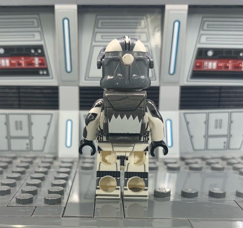 Puede incluir: Una minifigura Lego Star Wars de un clon de soldado gris y blanco con un casco y una mochila. La minifigura est&aacute; de pie sobre una superficie gris.