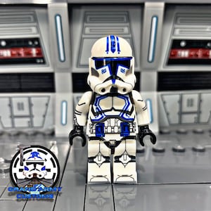 May include: A white and blue Lego minifigure of a Star Wars clone trooper. The figure has a blue helmet with white stripes and a blue and white torso with a black belt. The figure is standing on a grey surface.