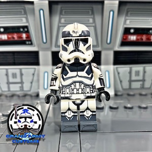 Könnte beinhalten: Eine weiße und schwarze LEGO-Minifigur eines Star Wars Klon-Soldaten. Die Figur hat einen schwarzen Helm mit einem weißen Streifen und einem weißen Symbol auf der Vorderseite. Die Figur trägt eine schwarz-weiße Rüstung und hat ein schwarzes Blastergewehr.