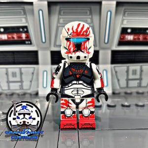 May include: A custom-painted LEGO minifigure of a clone trooper with a white and red helmet and black and white armour. The figure has a red and white paint scheme with a black and white design on the armour. The figure is standing on a grey surface.