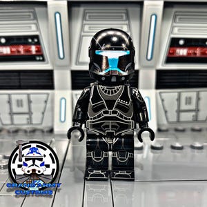 Könnte beinhalten: Eine schwarze und silberne Lego-Minifigur eines Star Wars Klon-Soldaten mit einem blauen Visier. Die Minifigur steht auf einer grauen Oberfläche.