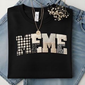 Peut inclure: Sweat-shirt noir à col rond avec le mot « MEME » en lettres patchwork. Les lettres présentent divers motifs, notamment du vichy, des rayures et des pois. Un collier en or avec un pendentif est drapé sur le sweat-shirt.