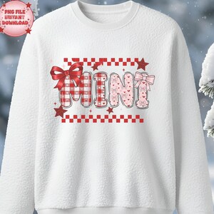 May include: White sweatshirt with the word "MINI" in a playful design. The letters are decorated with bows, hearts, and a red and white checkered pattern. Red stars and a checkered border complete the design.