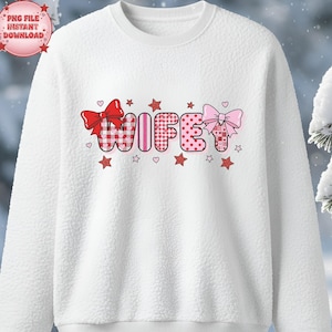 Peut inclure: Sweat-shirt blanc avec le mot "WIFEY" dans un design fantaisiste. Les lettres sont décorées de nœuds, de cœurs et d'étoiles rouges et roses. Le sweat-shirt a un aspect texturé et flou.