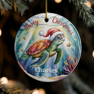 May include: A round Christmas ornament featuring a sea turtle wearing a Santa hat, swimming underwater. The ornament has the words "Merry Christmas" and "Charles 2025" on it. The background includes fish and coral.