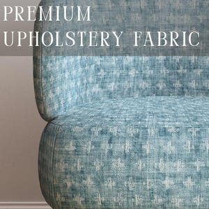 May include: A chair upholstered in blue fabric with a white cross-stitch pattern. The text PREMIUM UPHOLSTERY FABRIC is displayed at the top, and APOSTROFO DESIGN is at the bottom. The chair features light-coloured wooden legs and a curved backrest.