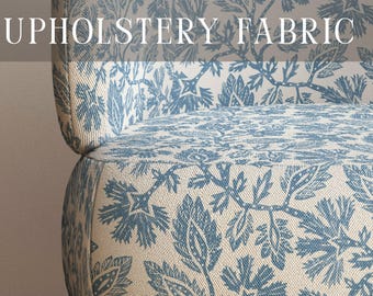 May include: A chair upholstered in a cream-colored fabric featuring a blue botanical floral pattern. The text PREMIUM UPHOLSTERY FABRIC is visible at the top, and APOSTROFO DESIGN is printed at the bottom. The chair has light brown wooden legs.