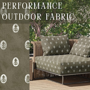 May include: Performance outdoor fabric featuring a repeating white botanical motif on a dark olive green background. The textile is shown applied to a cushioned outdoor sofa with a woven frame, displaying the pattern on the seat and back cushions.